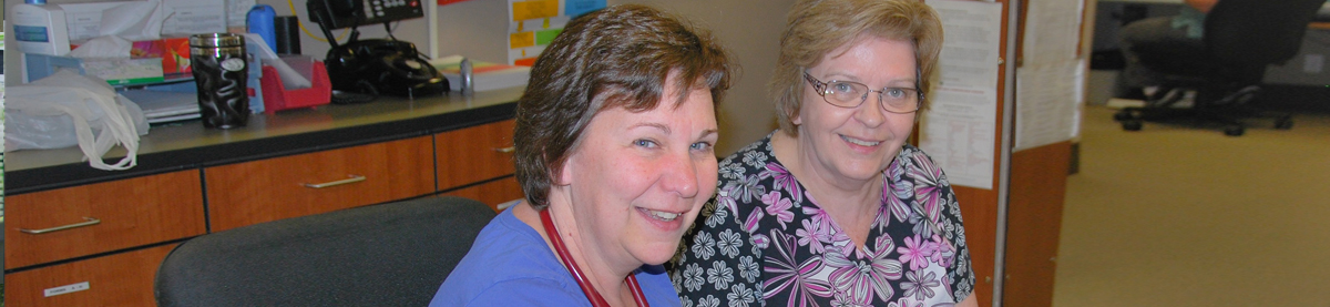 Two hospital employees at a desk smiling to camera